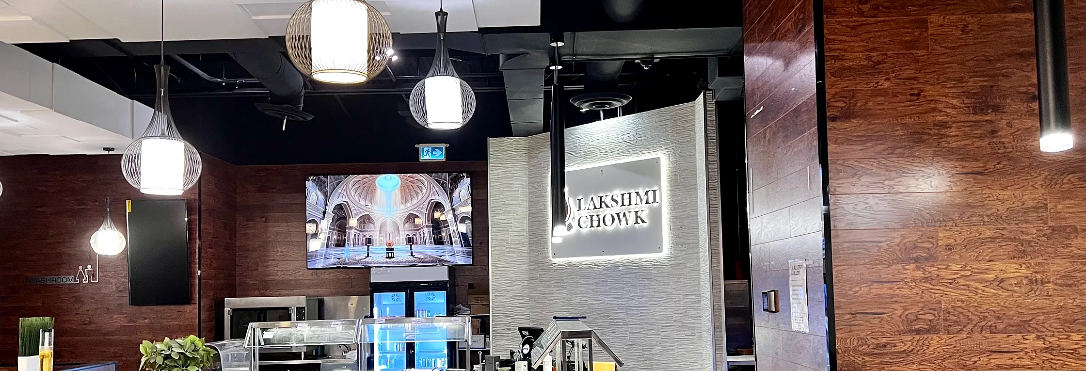 Inside Lakshmi Chowk in Ancaster: pendant lights, wood panelling and the lit Lakshmi Chowk sign