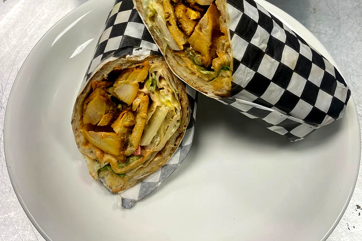 Chicken wrap cut in half and wrapped in checkered paper on a white plate