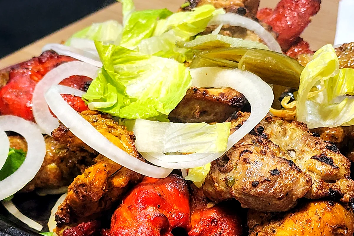 Mixed BBQ platter of chicken tikka, malai tikka, tandoori chicken and kababs on a sizzling plate with onions and lettuce