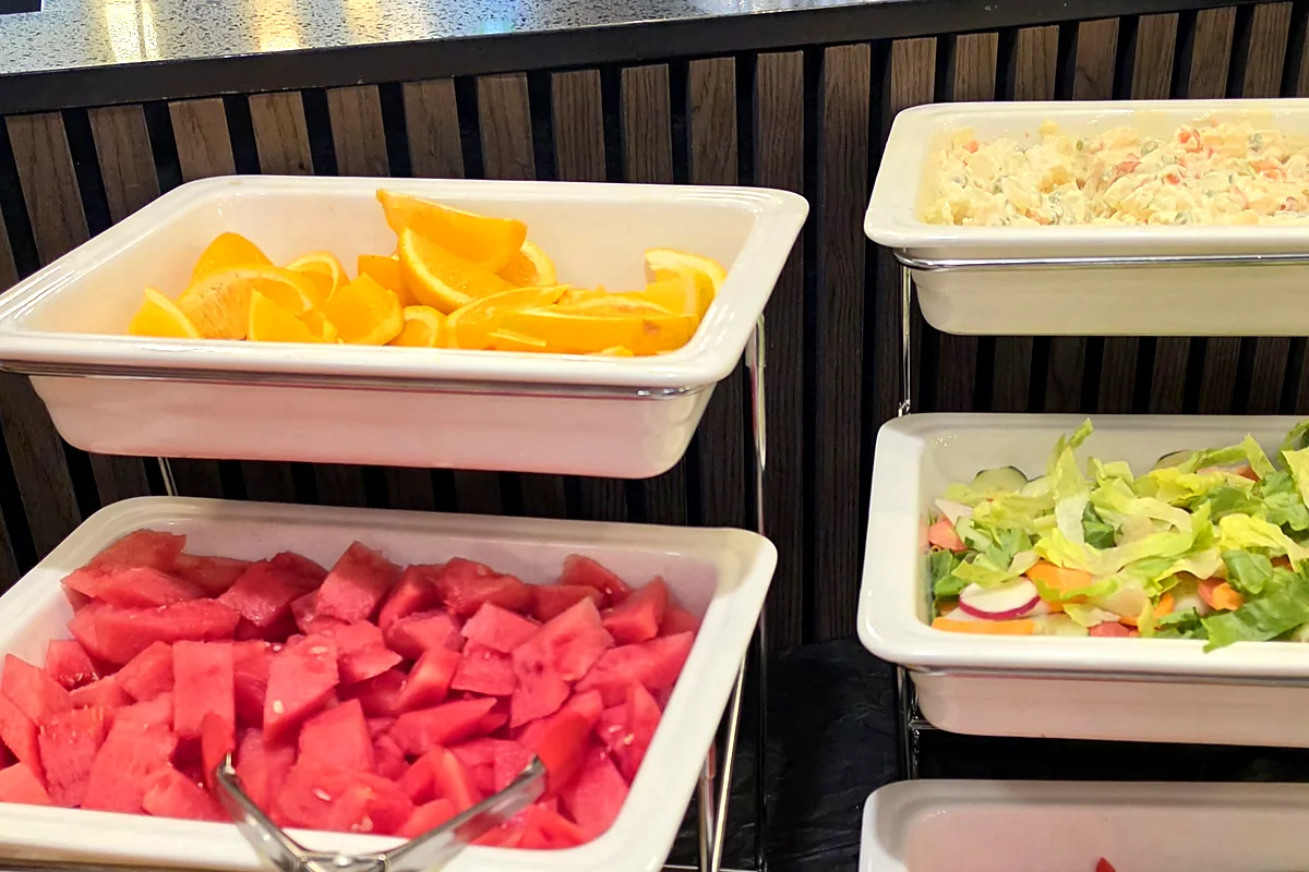 Buffet table with orange slices, watermelon, salad and side dishes in white trays